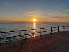 A sunset over the ocean with a concrete walkway and metal railing.