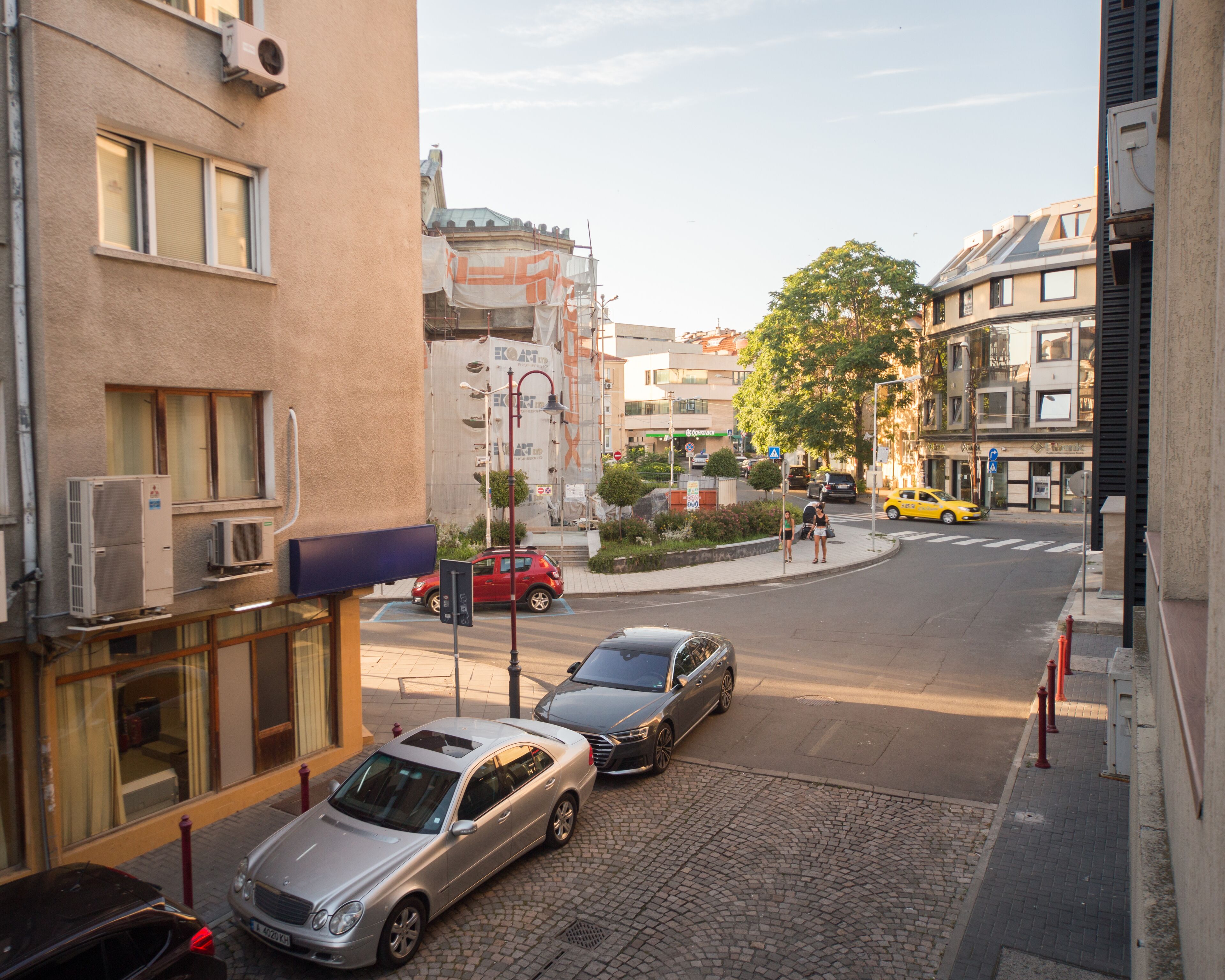 A street view with parked cars, buildings, and a yellow taxi.