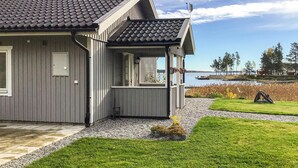 Ein modernes Haus mit grauer Fassade, einem Ziegeldach und einer Veranda mit Blick auf einen See.