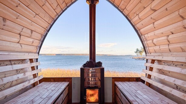 Eine Holzhütte mit einem zentralen Kamin, Bänken und Blick auf einen See.