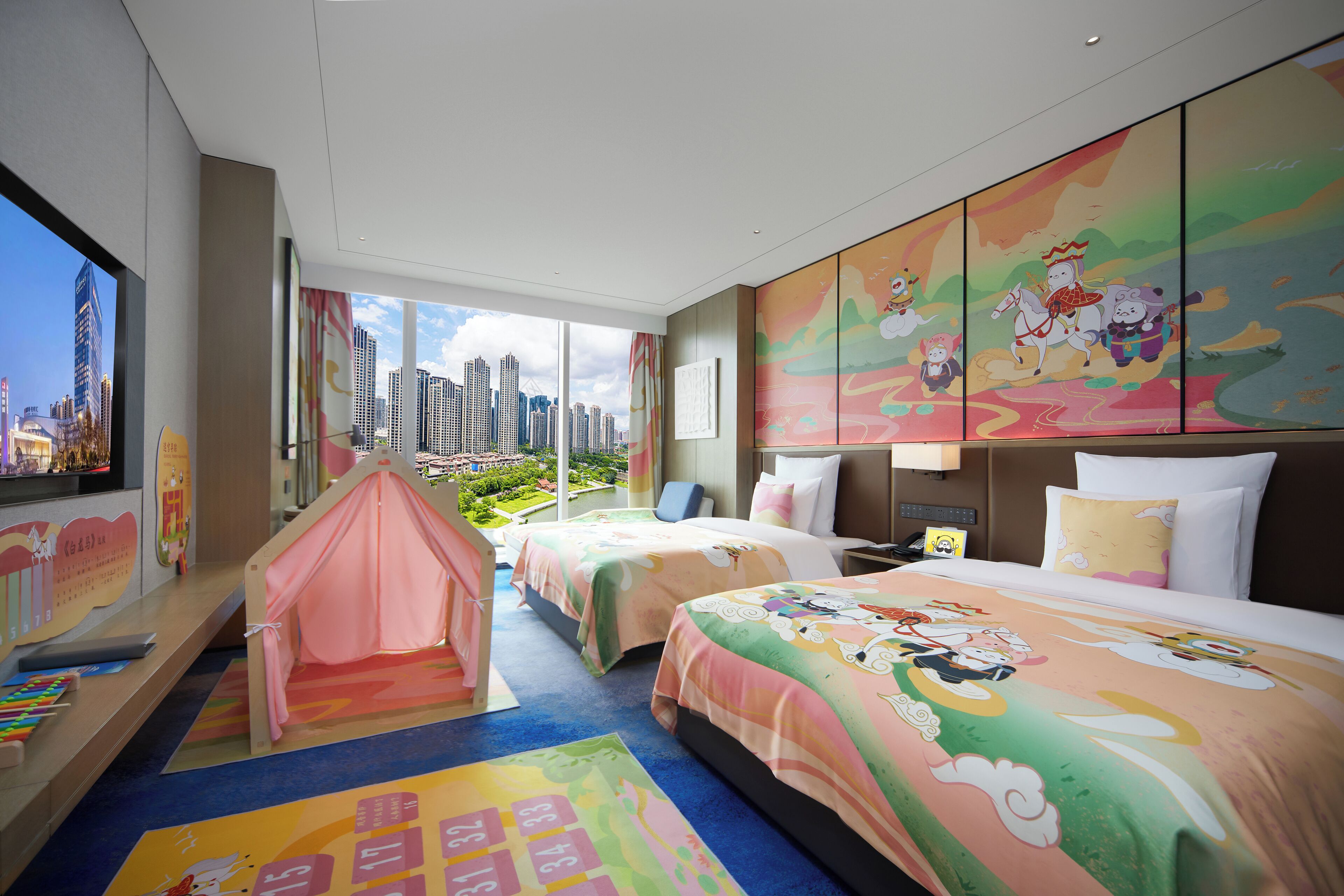 A hotel room with a city view, two beds, a play tent, and colorful artwork on the walls.
