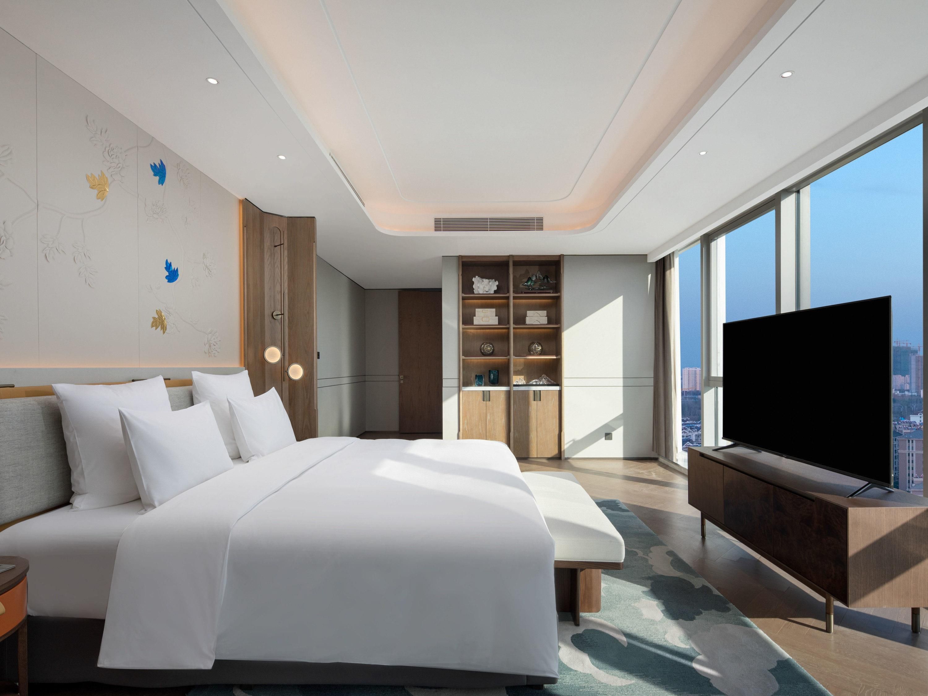 Ein modernes Hotelzimmer mit einem großen Bett, einem eingebauten Kleiderschrank, einem Fernseher und Blick auf die Stadt.