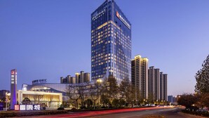A high-rise hotel with a modern glass facade, surrounded by other buildings and a well-lit street. - Pullman Huai’an (Huai'an)