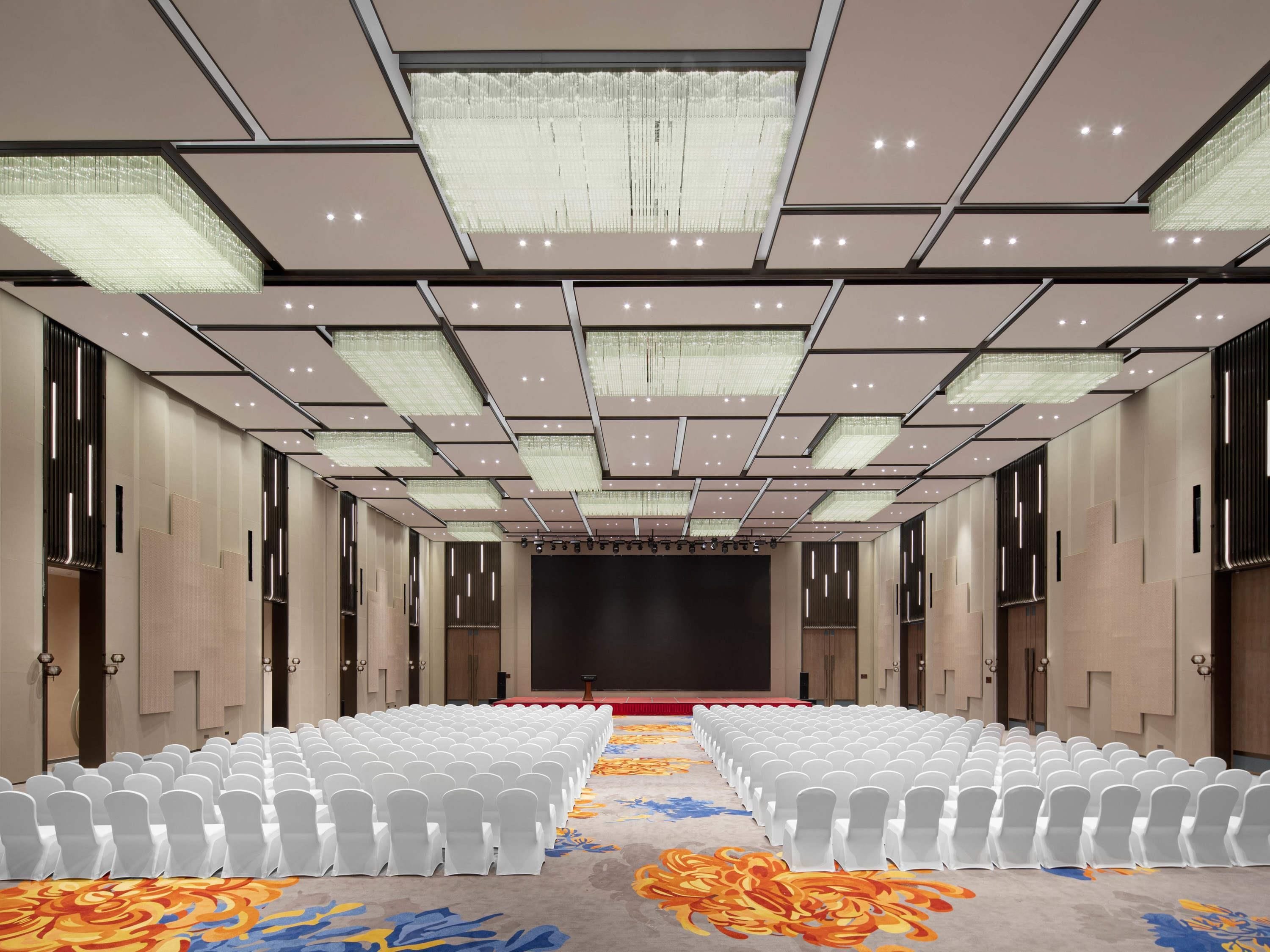 A conference room with rows of white chairs, a stage, and a patterned carpet.