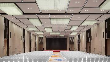 A conference room with rows of white chairs, a stage, and a patterned carpet.