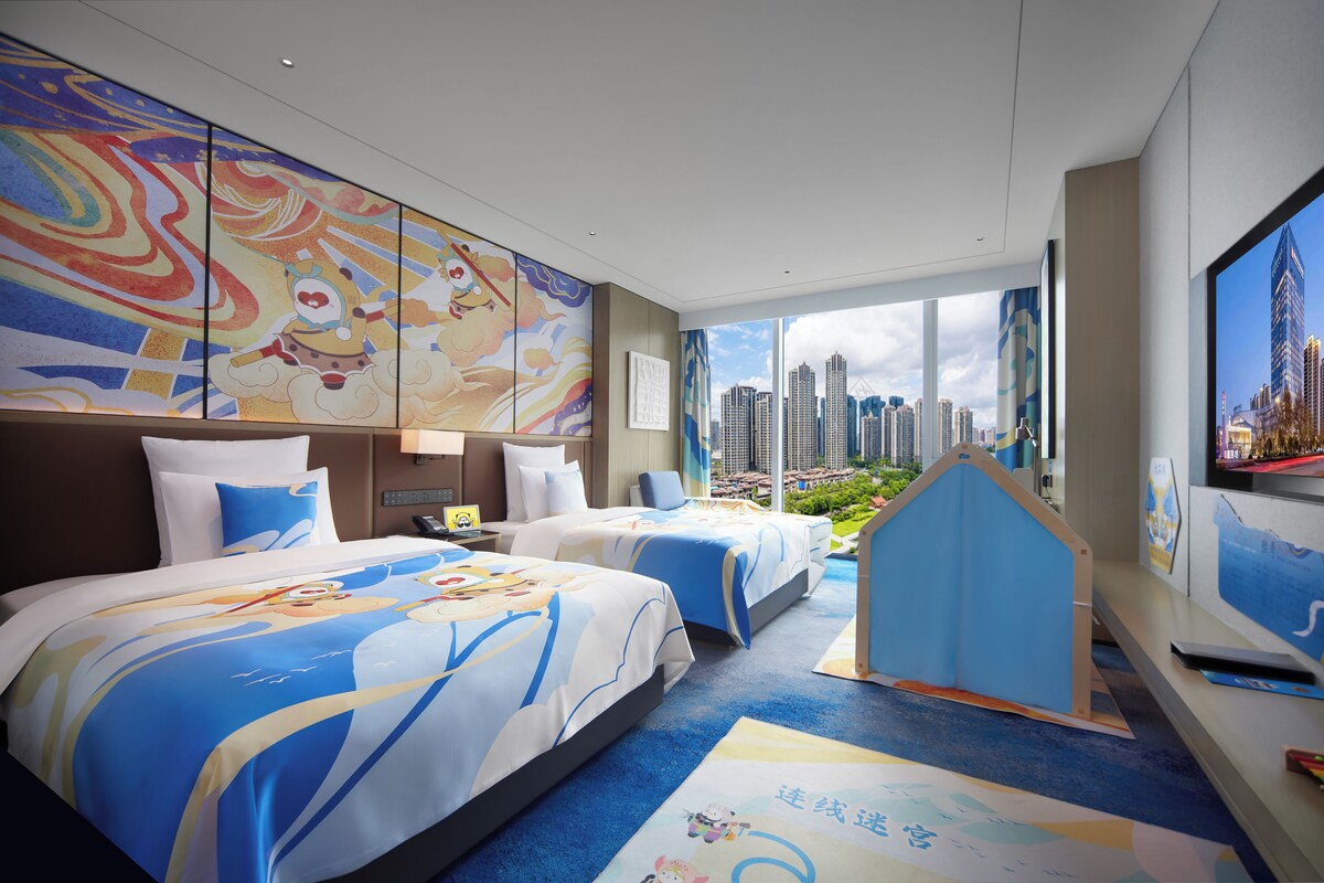 Ein Hotelzimmer mit zwei Betten, Blick auf die Stadt und einem farbenfrohen Wandgemälde.