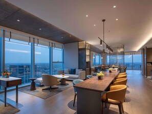 Un intérieur moderne avec une longue table à manger, des sièges confortables et de grandes fenêtres offrant une vue sur la ville.
