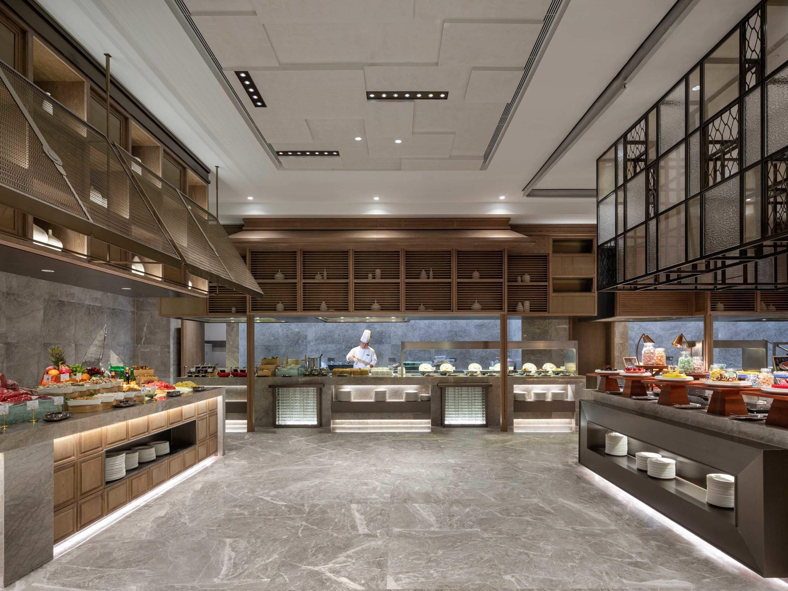 Een moderne buffetopstelling met een kok die eten bereidt, marmeren vloeren en houten planken.
