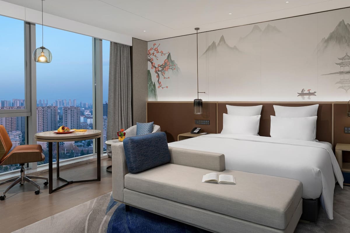 Ein modernes Hotelzimmer mit einem großen Bett, einem Schreibtisch, einem Stuhl und Blick auf die Stadt.