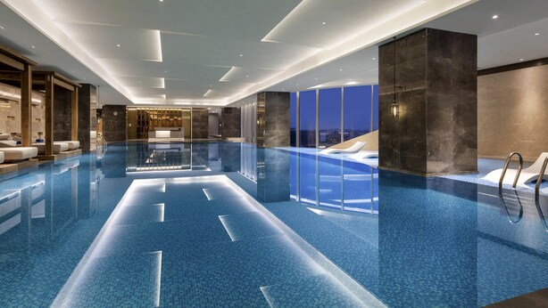 A modern indoor swimming pool with clear water, a reception area, and a view of the city at night. - Pullman Huai’an (Huai'an)