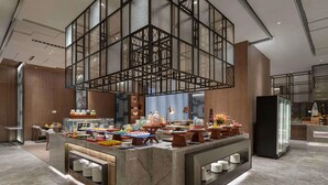 A modern hotel lobby with a central buffet area, marble flooring, and a high ceiling with a geometric glass structure. - Pullman Huai’an (Huai'an)