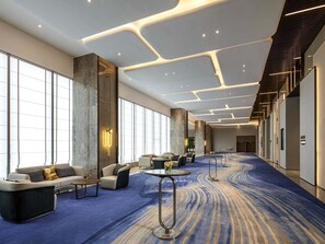 A modern hotel lobby with a blue carpet, seating areas, and large windows. - Pullman Huai’an (Huai'an)