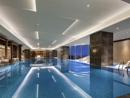 A modern indoor swimming pool with clear lines, a reception area, and a view of the city at dusk.. Pullman Huai’an