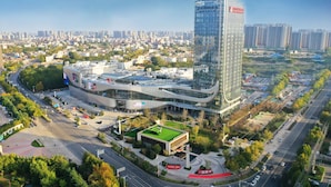 A modern hotel with a prominent glass facade, surrounded by a landscaped area and a busy urban street. - Pullman Huai’an (Huai'an)