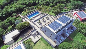 An aerial view of a modern building with a swimming pool, solar panels, and lush greenery.