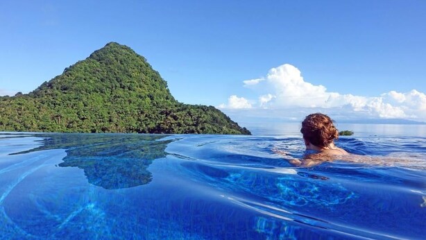 A person in a clear blue infinity pool with a view of a lush green island. - Coulibri Ridge (Soufriere)