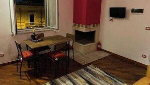 A room with a wooden dining table, red upholstered chairs, a fireplace, a TV mounted on the wall, and a large window with an open view of a building at night. - La Piccola Terrazza - Santo Spirito well connected with Bari (Bari)