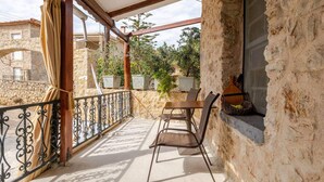 A balcony with a table and chairs, a window, and a view of a stone building and trees. - Serenity Villa Retreat in Pidasos (Pylos-Nestoras)