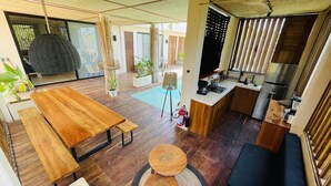 Eine moderne Küche mit Einbauherd, Spüle und Kühlschrank. Ein Essbereich mit Holztisch und Bänken lädt zum Verweilen ein. Das Zimmer verfügt über ein großes Fenster und einen Deckenventilator.