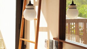 Ein Schlafzimmer mit einer Holzleiter, die an einer Wand lehnt, einem Bett mit weißer Bettwäsche und zwei Pendelleuchten.