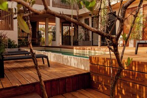 Un espace piscine agrémenté d’une terrasse en bois, de chaises longues et de plantes en pot.