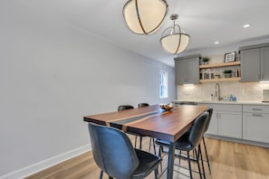 A modern kitchen with a wooden dining table, two chairs, and pendant lighting.