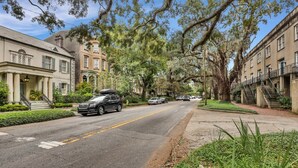 A street lined with historic buildings, a black SUV parked on the side, and a clear blue sky.
