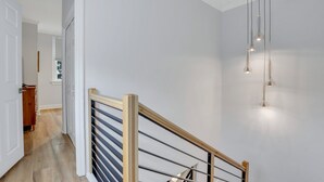 A staircase with a wooden handrail and a glass balustrade, leading to a room with white walls and a ceiling light fixture.