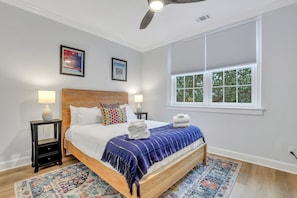 A bedroom with a wooden bed, two bedside tables with lamps, a window with blinds, and two framed pictures on the wall.