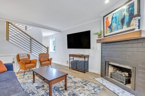 A modern living room with a fireplace, a mounted TV, and a staircase.