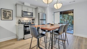 A modern kitchen with grey cabinets, stainless steel appliances, and a wooden dining table with bar stools.