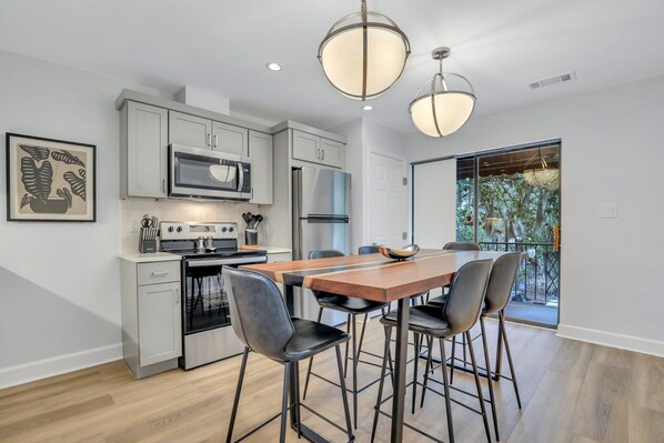 A modern kitchen with grey cabinets, stainless steel appliances, and a wooden dining table with bar stools.