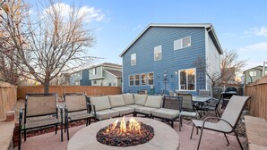 A backyard with a stone fire pit, outdoor furniture, and a blue house in the background. - Ideal for Families & Groups | Theatre | Pet Friendly | Firepit | Spacious (Brighton)
