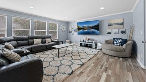 A modern living room with a sectional sofa, a round coffee table, and a flat-screen TV mounted on the wall. - Ideal for Families & Groups | Theatre | Pet Friendly | Firepit | Spacious (Brighton)