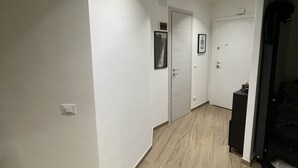 Un couloir doté d’un plancher en bois, de murs blancs et de luminaires encastrés au plafond. On y trouve deux portes, dont l’une est surmontée d’un tableau accroché au mur.