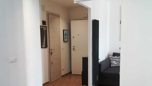 Un couloir avec un plancher en bois, des murs blancs et un canapé noir à l’arrière-plan.