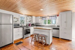 A kitchen with white cabinets, a wooden ceiling, and a central island with stools. - Enjoy your own home in Hampton Falls! (Hampton Falls)