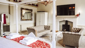 A bedroom with a four-poster bed, two armchairs, a sofa, a fireplace, a TV, and a large mirror. - The Old Crown Coaching Inn (Faringdon)