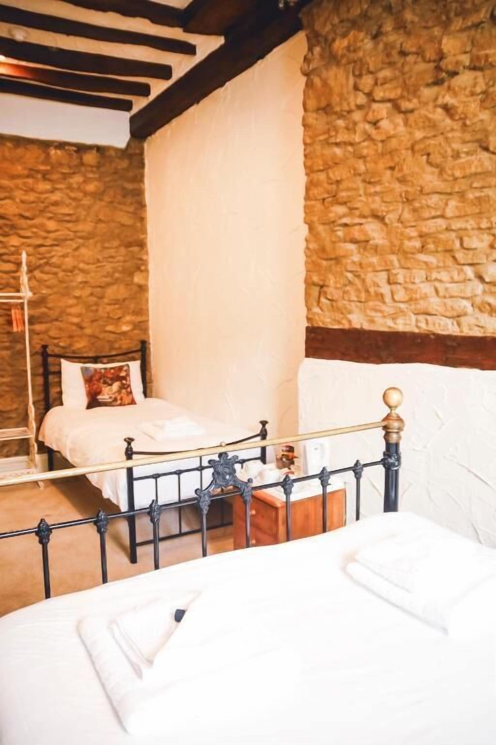 Een slaapkamer met een stenen muur, een bed met een houten hoofdbord en een metalen bedframe.