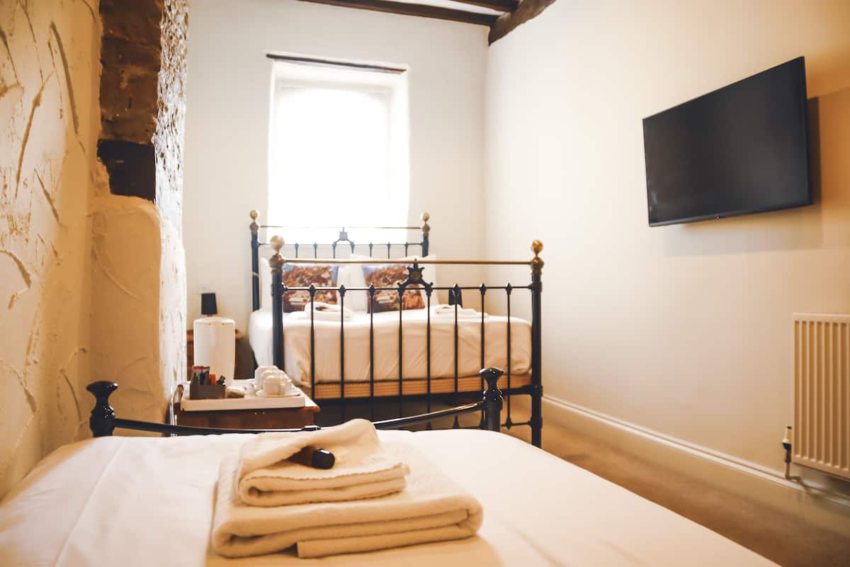 A bedroom with a bed, a bedside table, a window, a wall-mounted TV, and a radiator.