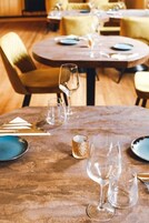 Un comedor con mesas redondas dispuestas para dos comensales, cada una con una copa de vino, un vaso de agua y cubiertos.