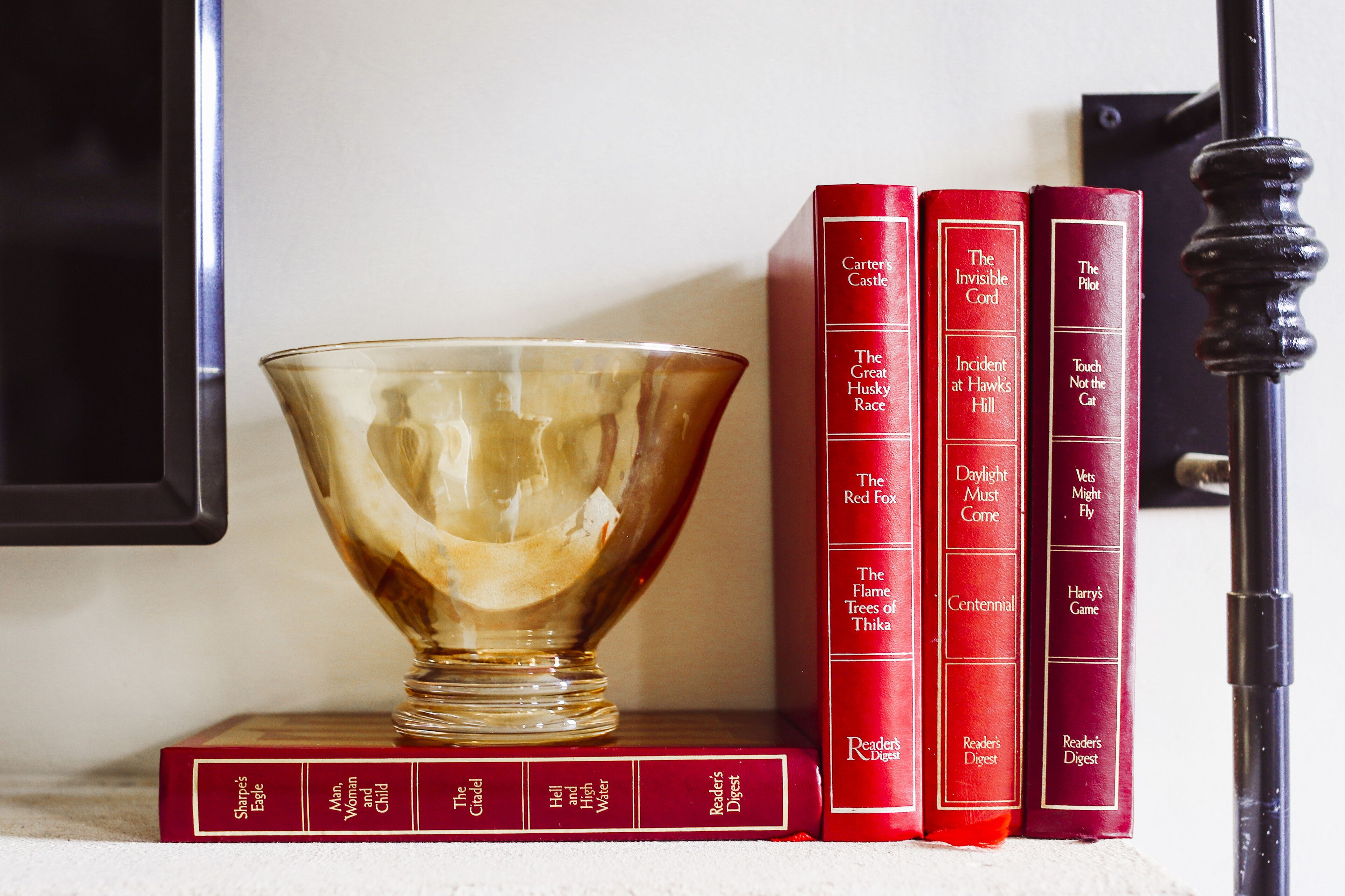 Una colección de libros rojos en una estantería, con un cuenco de vidrio transparente al frente.