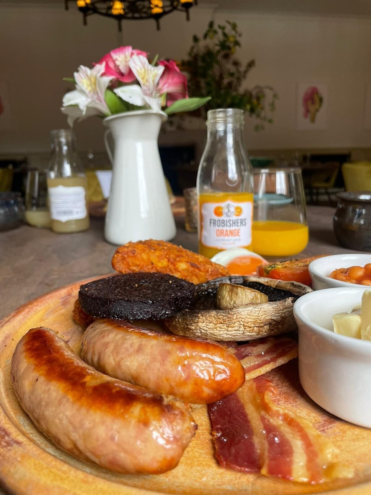 Una tabla de madera con diversos embutidos, incluyendo salchichas y tocino, y una botella de jugo de naranja.