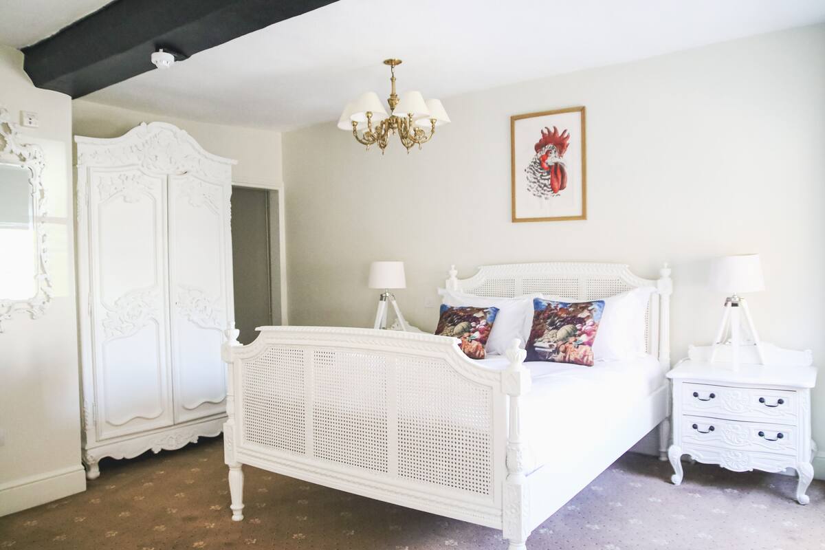A white four-poster bed with a canopy, a white nightstand with drawers, a white wardrobe, and a chandelier.