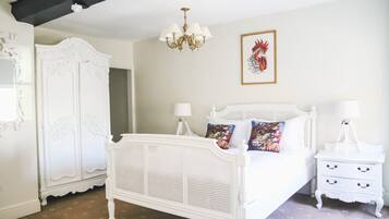Uma cama de casal branca com dossel, uma mesa de cabeceira branca com gavetas, um guarda-roupa branco e um candelabro.