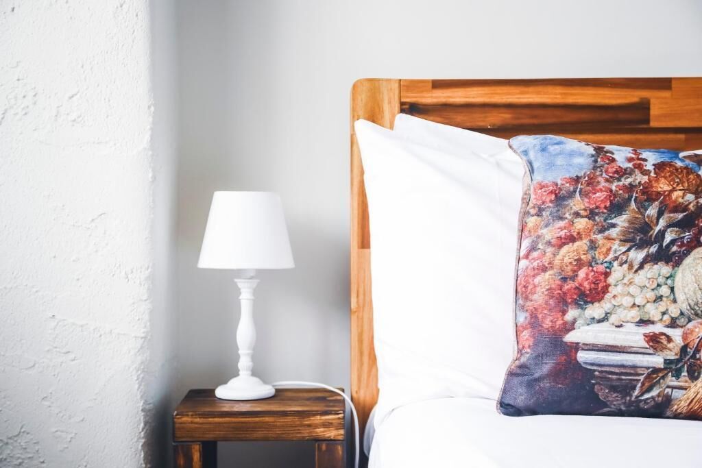 A neatly made bed with a wooden headboard, a white pillow, and a small bedside table with a white lamp.