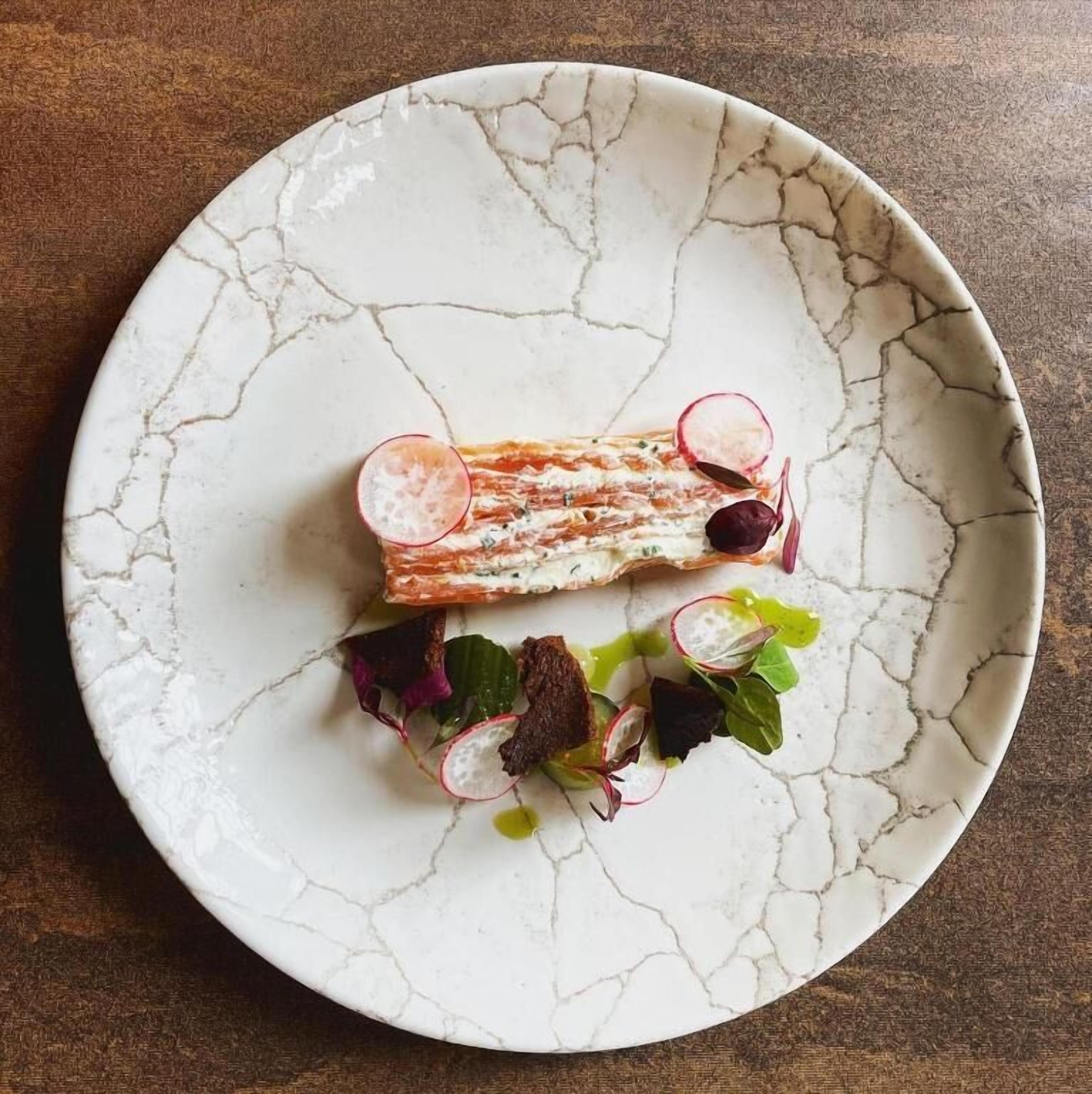 Un plato con tartar de salmón, rodajas de rábanos y verduras de hoja.