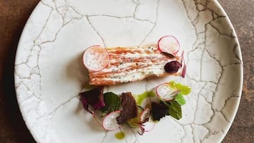 Un plato con tartar de salmón, rodajas de rábanos y verduras de hoja.