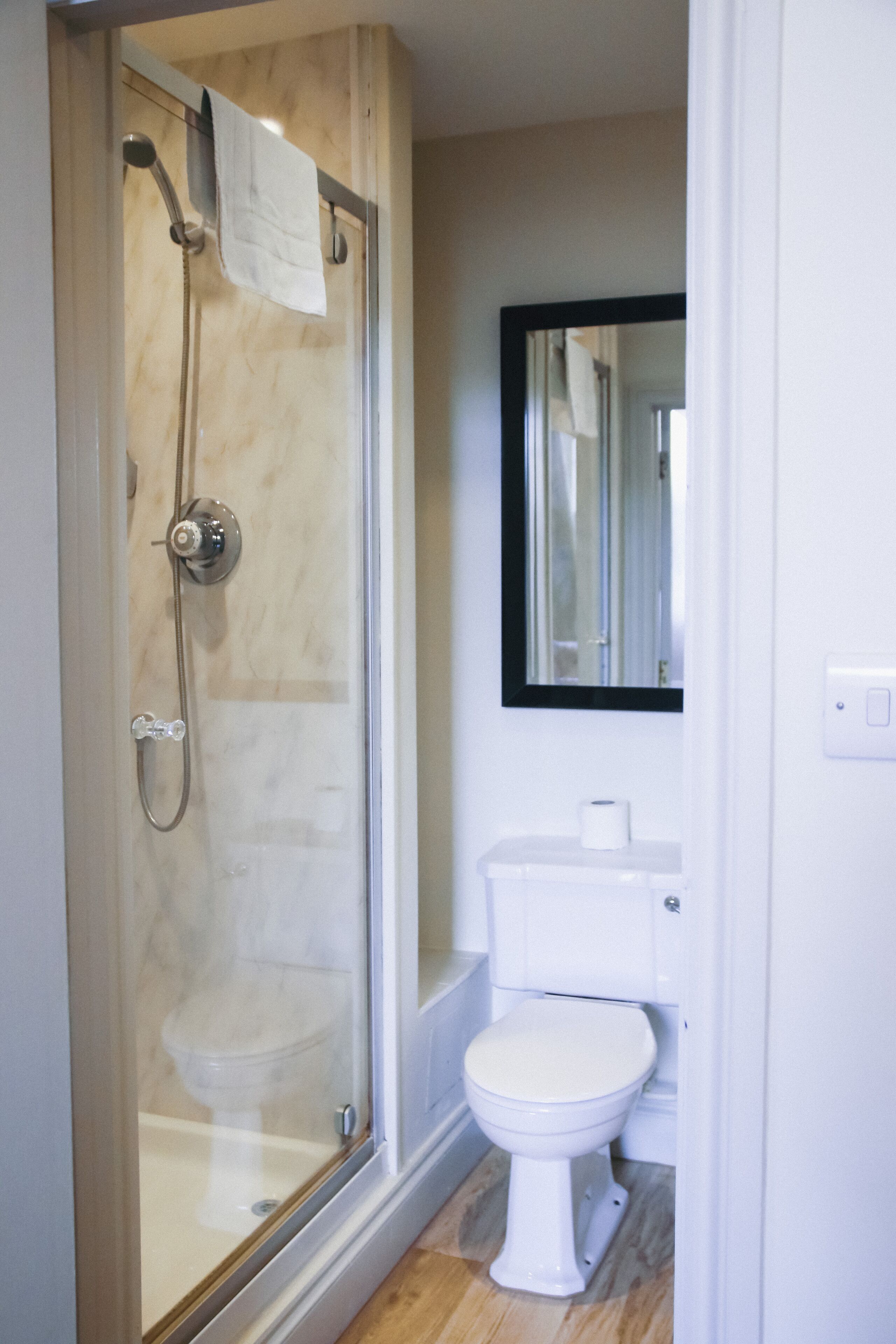 Une salle de bain avec une douche à parois de verre, des toilettes blanches et un miroir au-dessus du lavabo.