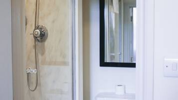 Une salle de bain avec une douche à parois de verre, des toilettes blanches et un miroir au-dessus du lavabo.